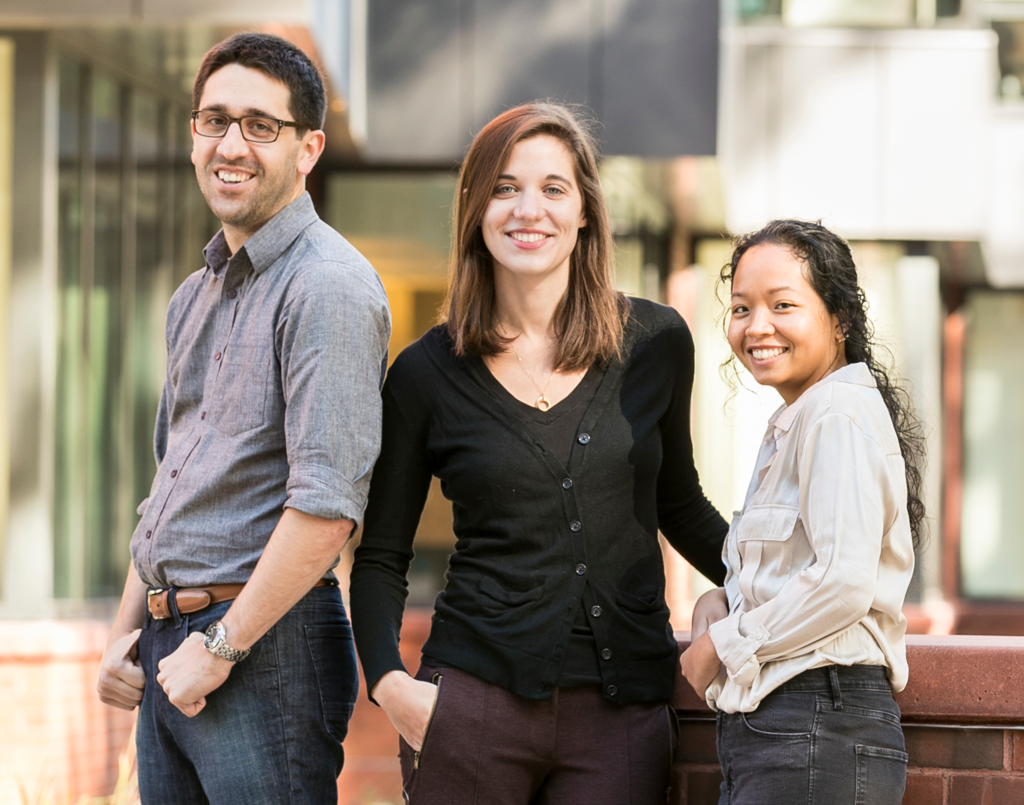 3 students stand together outside on Mason's campus, smiling at the camera