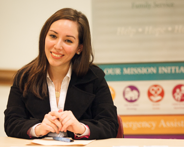 An employer sits at a table in front of a sign for their company